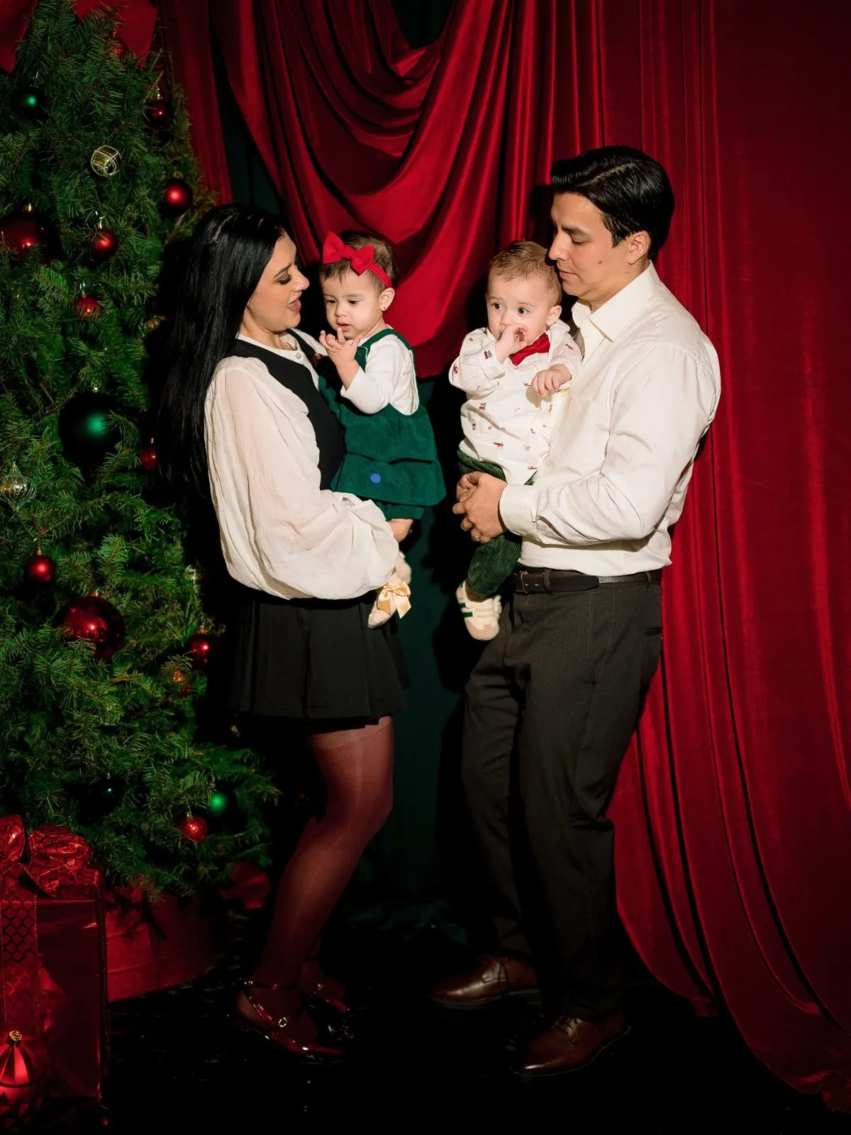 Familia con dos bebés frente a cortinas de terciopelo rojo y un pino decorado