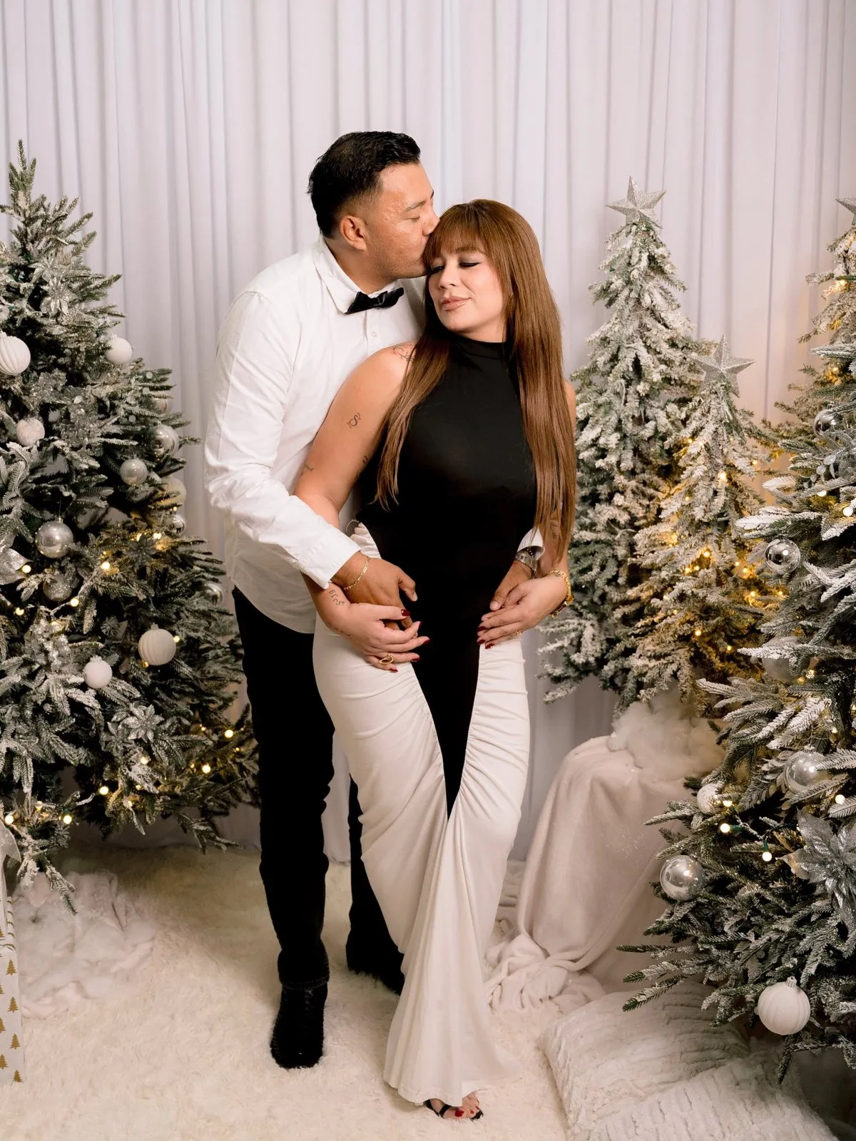 Pareja con ropa blanca y negra entre pinos nevados
